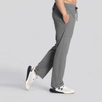 A person wearing gray drawstring jogger-style pants and white athletic sneakers, shown from the waist down in a studio setting with a light gray background.