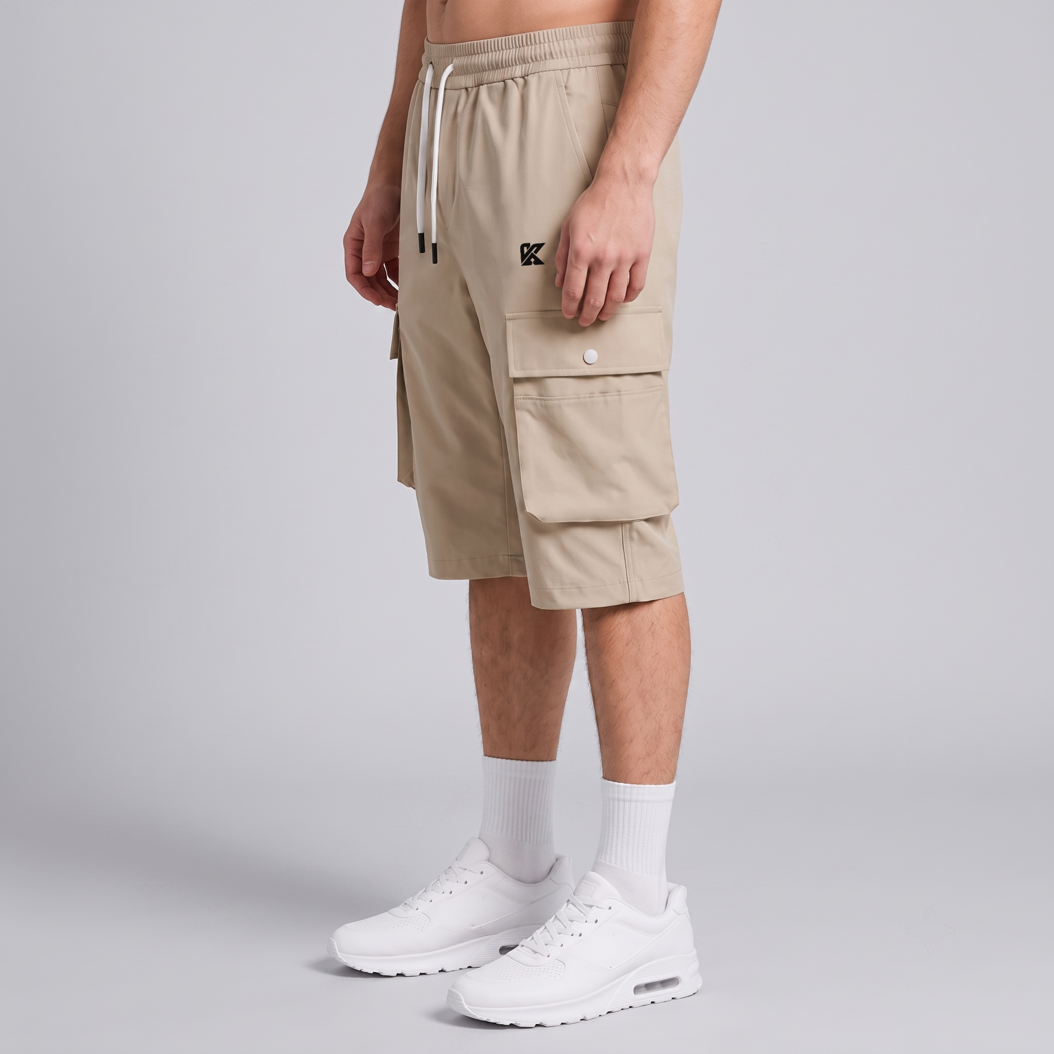 A model wearing beige cargo shorts with white drawstrings, white crew socks, and white sneakers, shown from the waist down against a light gray studio background.