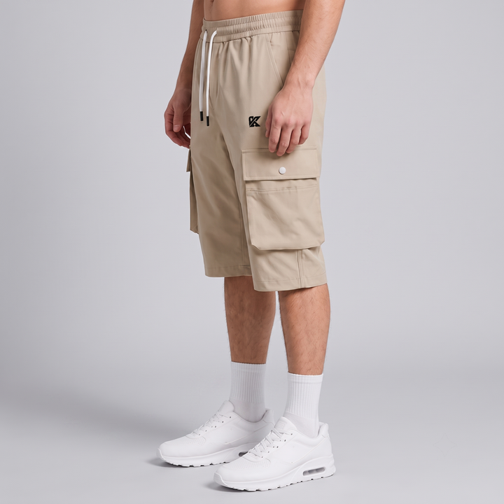 A model wearing beige cargo shorts with white drawstrings, white crew socks, and white sneakers, shown from the waist down against a light gray studio background.