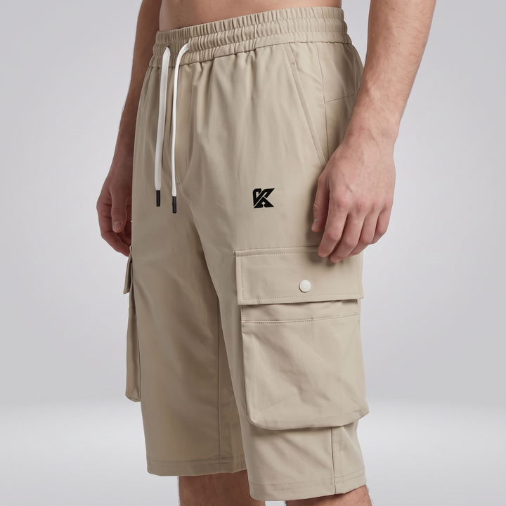 A person wearing beige cargo shorts with a white drawstring and a black embroidered logo on the left chest, photographed against a light gray studio background.