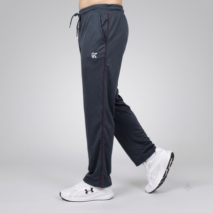 A person shown from the waist down wearing dark slate gray athletic sweatpants with a white embroidered logo on the left thigh and white Under Armour sneakers, captured against a light gray studio background.