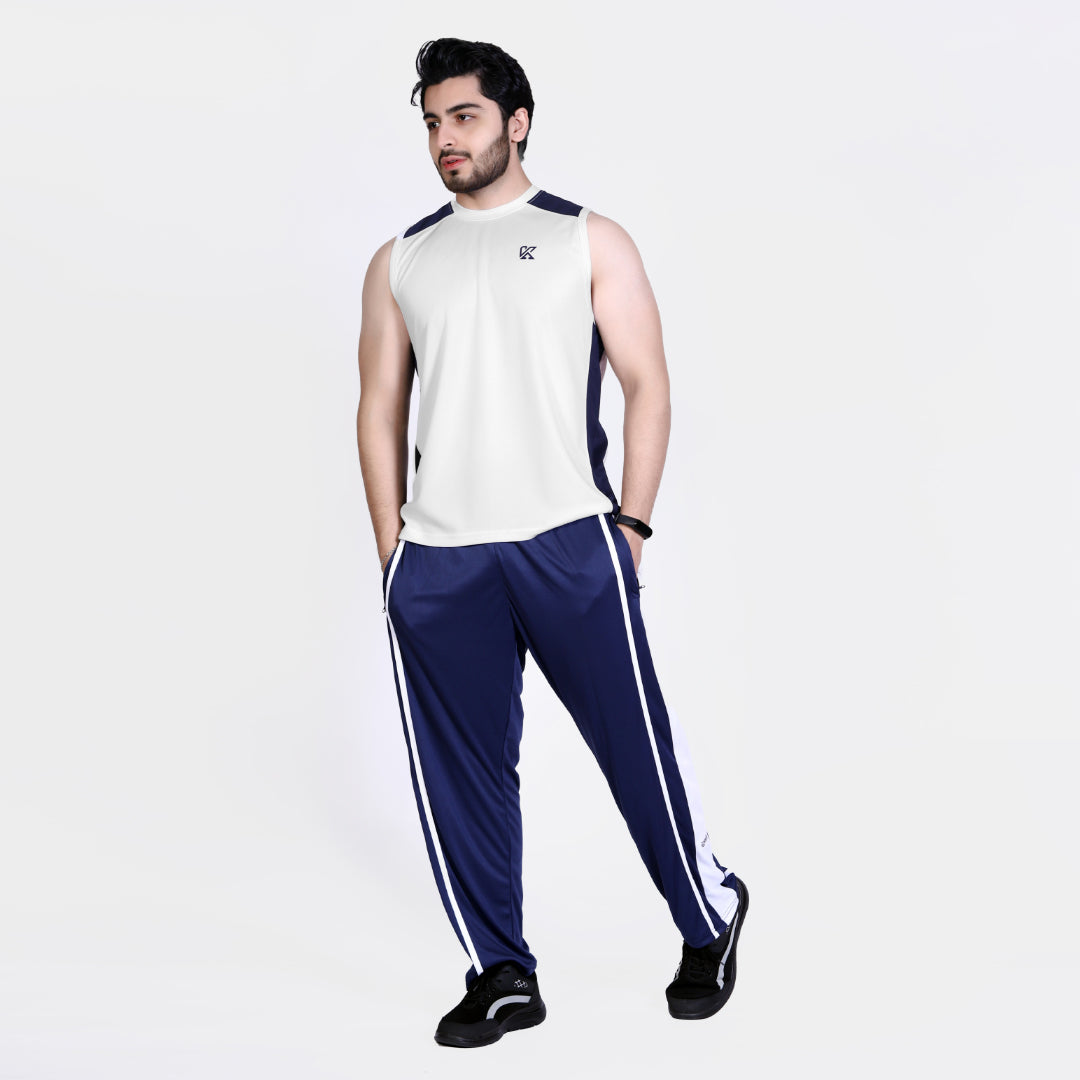 Man wearing a white sleeveless shirt and blue tracksuit with white stripes on a light gray background