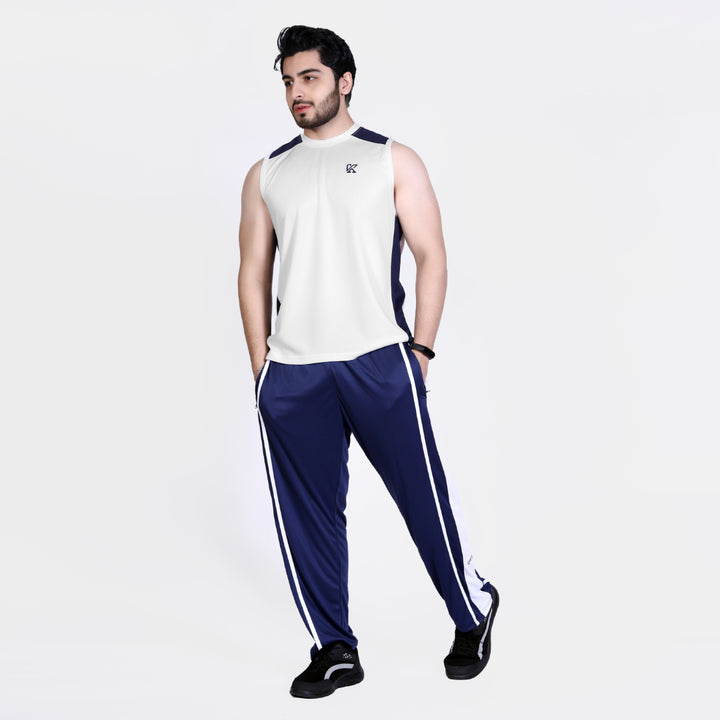 Man wearing a white sleeveless shirt and blue tracksuit with white stripes on a light gray background