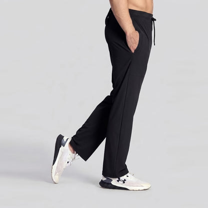 A side-profile view of a person wearing black drawstring athletic pants and white sneakers against a light gray studio background.