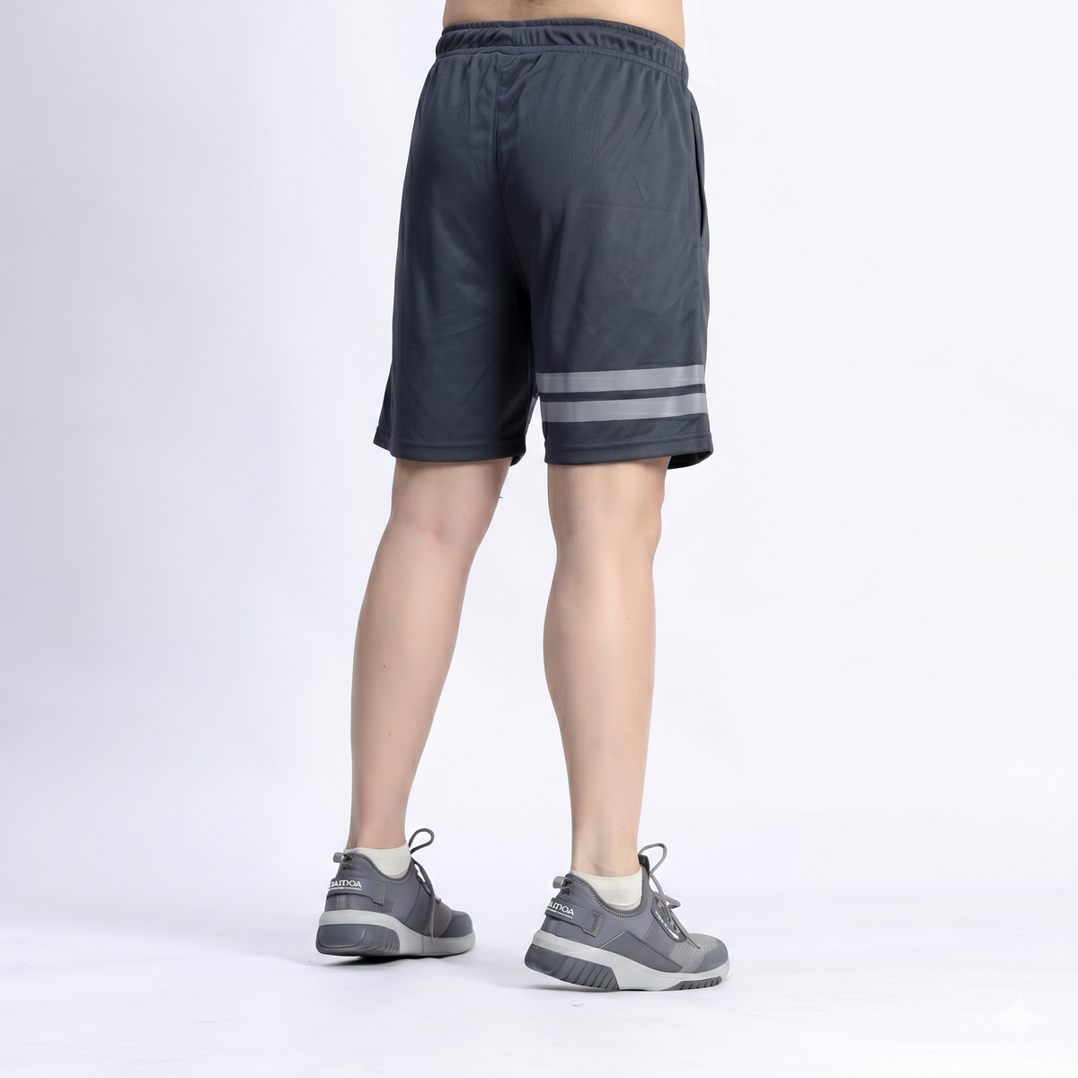 Person wearing dark gray shorts with reflective stripes on a white background
