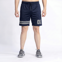 A person wearing navy athletic shorts with a drawstring waist, two horizontal gray stripes near the hem, and a large outlined '01' on the left leg, shown from the waist down against a light gray studio background.