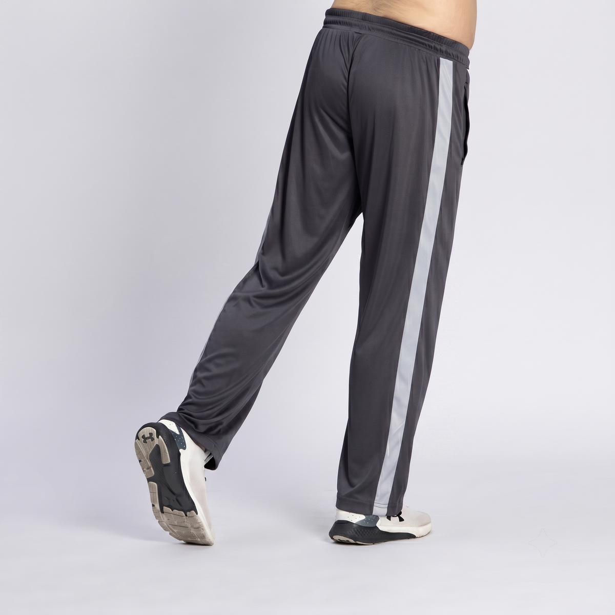 A person wearing dark gray athletic track pants with a light gray vertical stripe down the side, shown from the waist down against a light gray studio background.