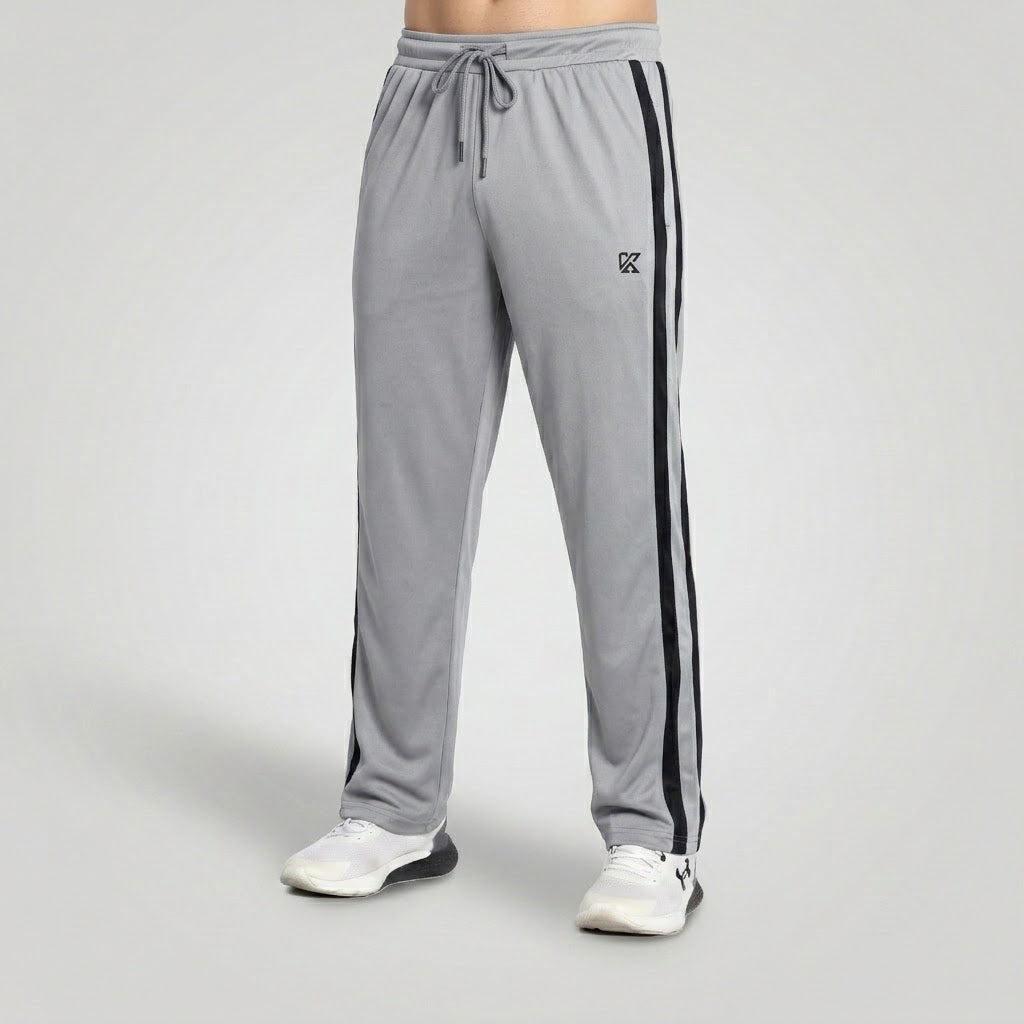 Gray athletic sweatpants with black side stripes and a small black logo on the left thigh, shown on a model from the waist down wearing white sneakers against a light gray studio background.