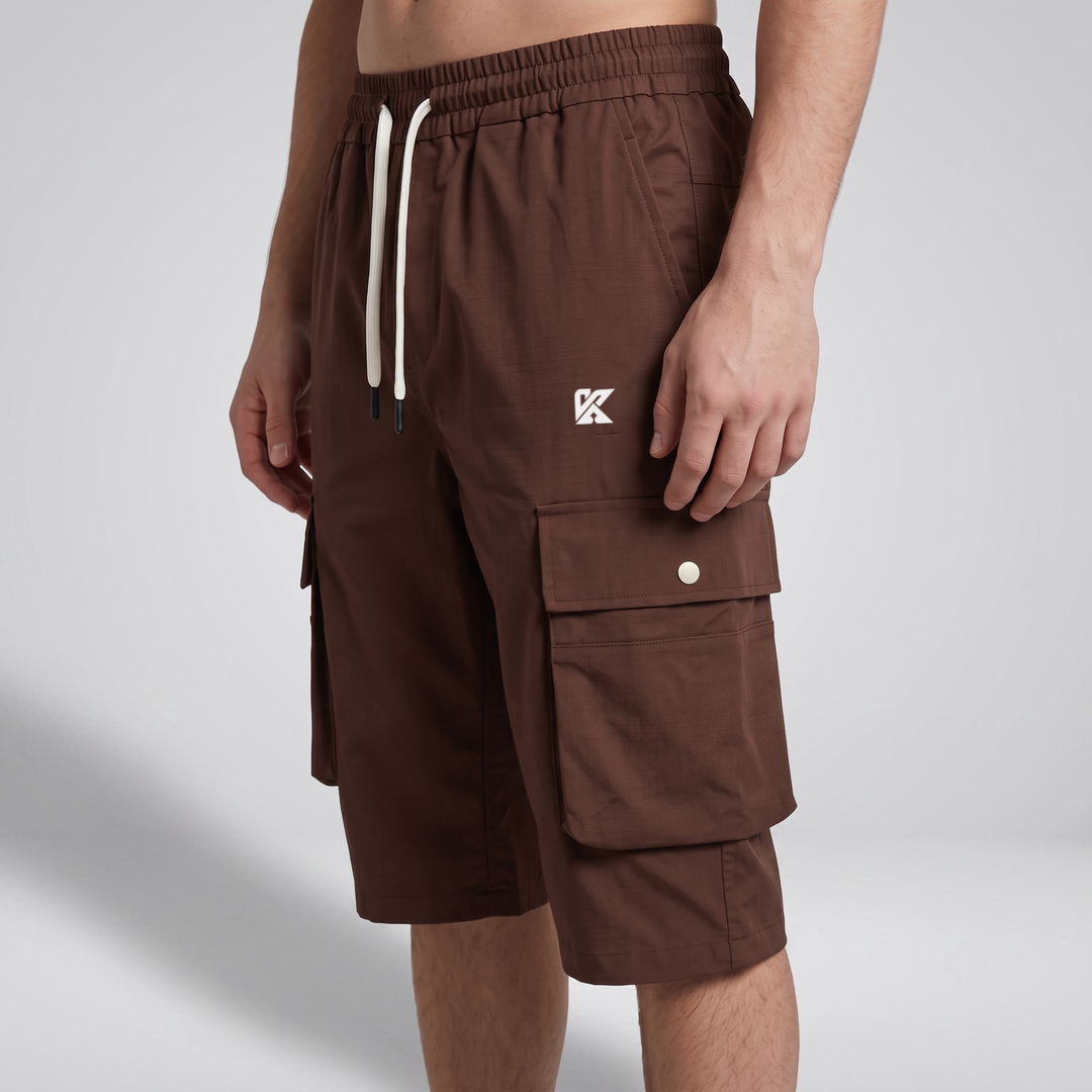 A person wearing brown cargo shorts with a white drawstring and a small white logo on the left thigh, photographed against a light gray studio background.