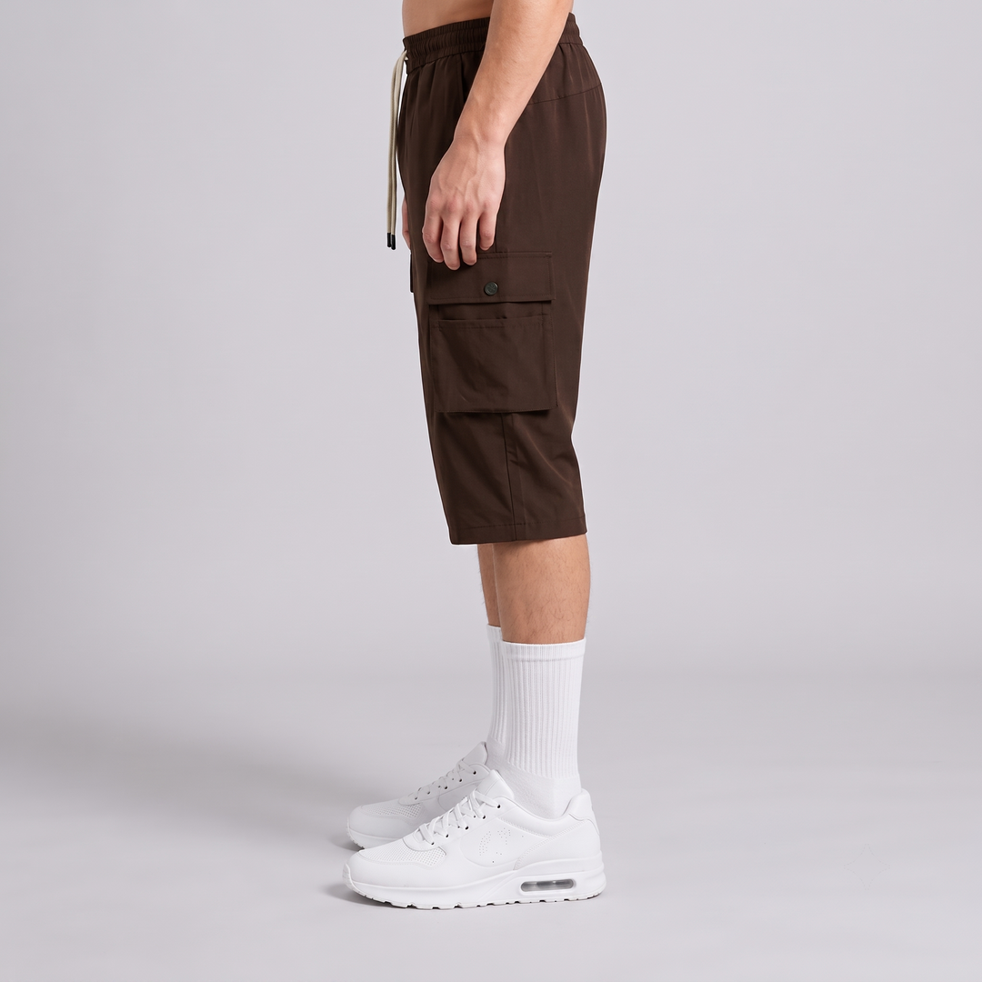 A side-profile studio shot of a model wearing dark brown cargo shorts, white crew socks, and white sneakers against a light gray background.