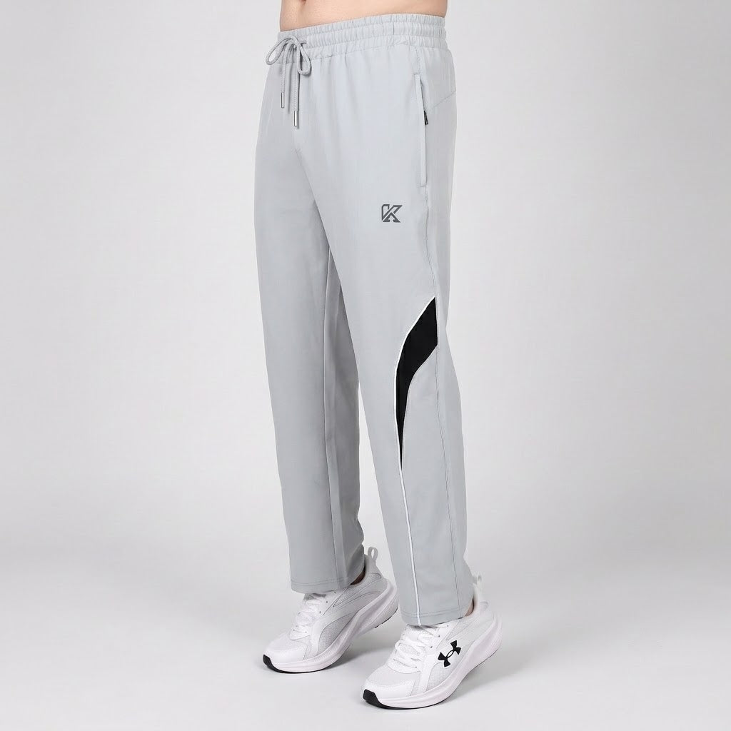 Light gray athletic jogger pants with a black side panel and a small black monogram logo on the left thigh, shown on a model wearing white sneakers against a light gray studio background.